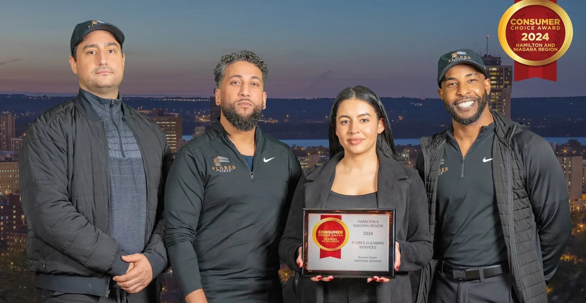 Four Flores Clean team members holding their 2024 Consumer Choice Award plaque, with the Hamilton skyline at dusk behind them