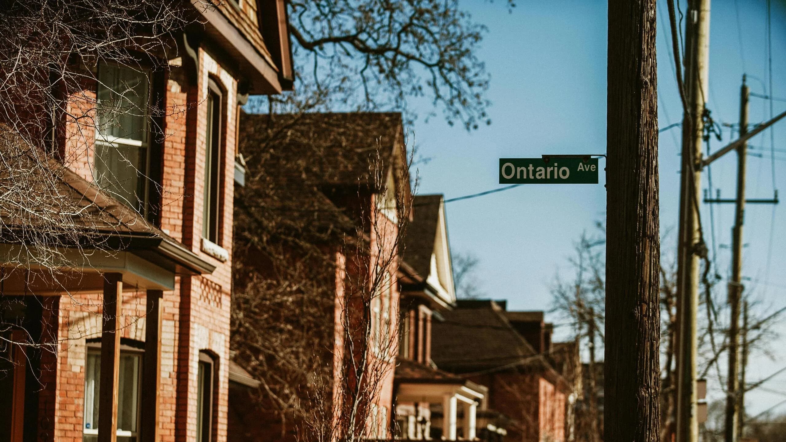 A quiet residential street lined with red-brick century homes beneath an 'Ontario Ave' street sign