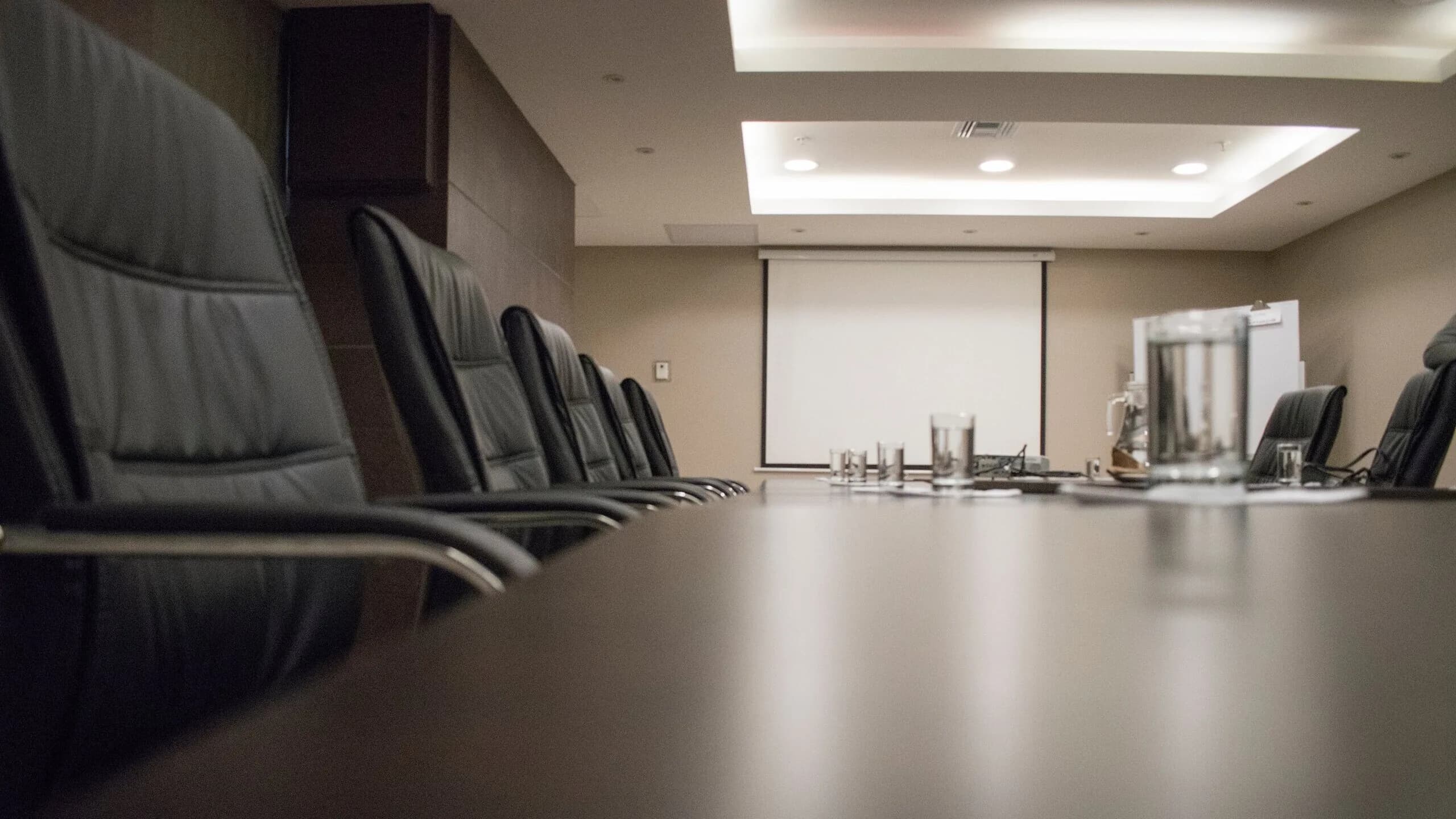 A clean, empty boardroom with black leather chairs lining a polished conference table
