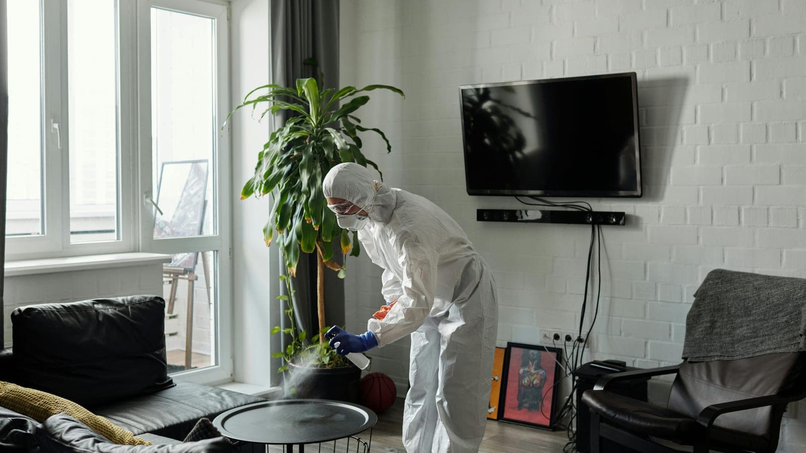 A technician in protective gear applying electrostatic disinfectant spray