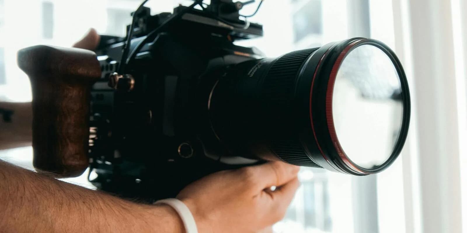 A camera operator holding a professional cinema camera with a large prime lens