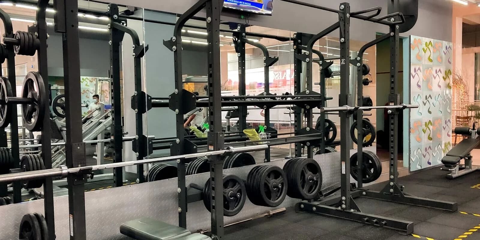 A commercial gym floor with a loaded squat rack, weight plates, and training benches