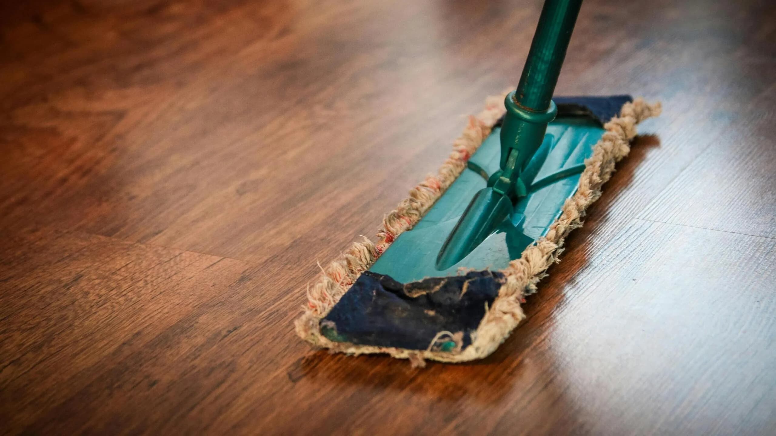A flat dust mop gliding across a polished dark hardwood floor