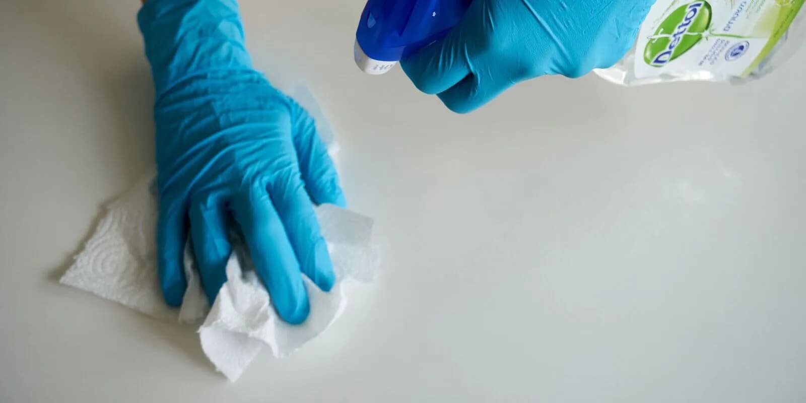 A gloved hand disinfecting and wiping down a clinical surface with sanitizing spray