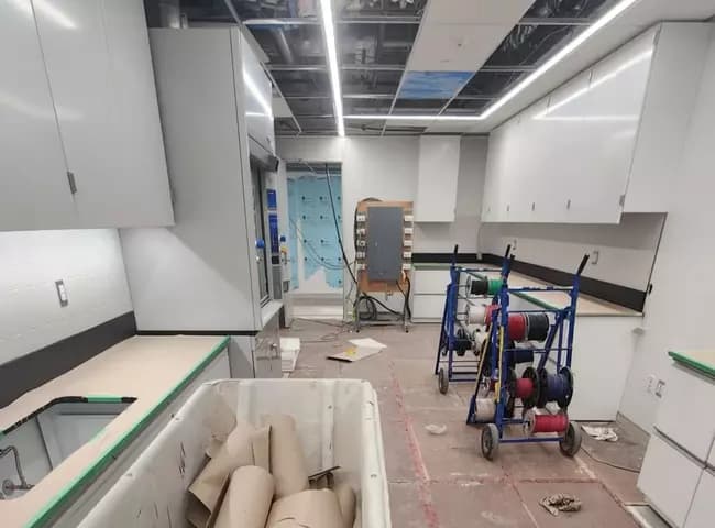 Commercial fit-out mid-construction with cabinetry, cable spools and debris before a post-construction clean