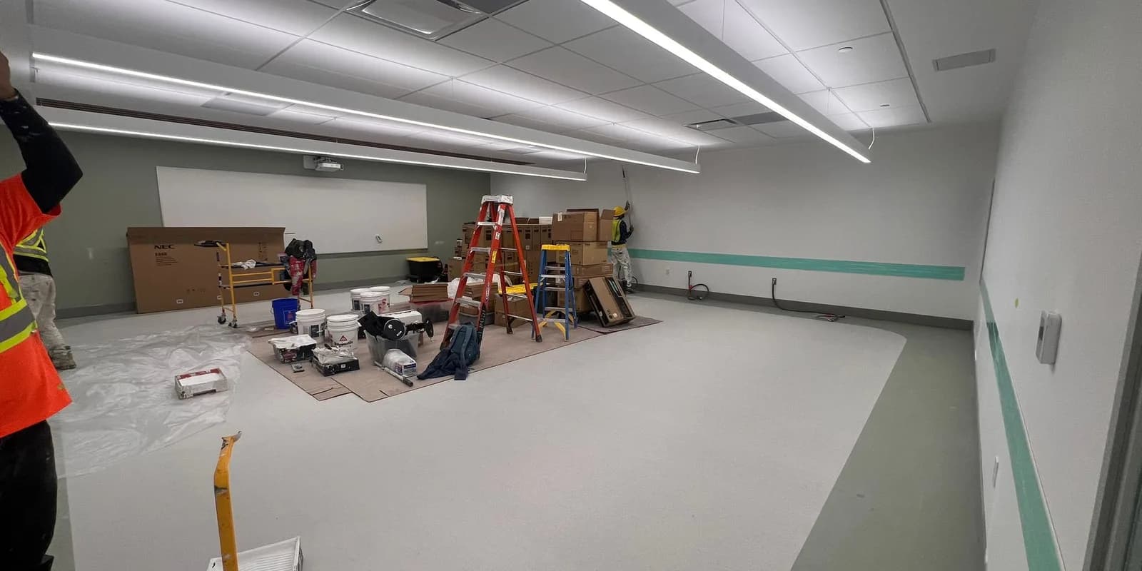 A newly built room being finished, with a worker, step ladders, and supplies on protected floors