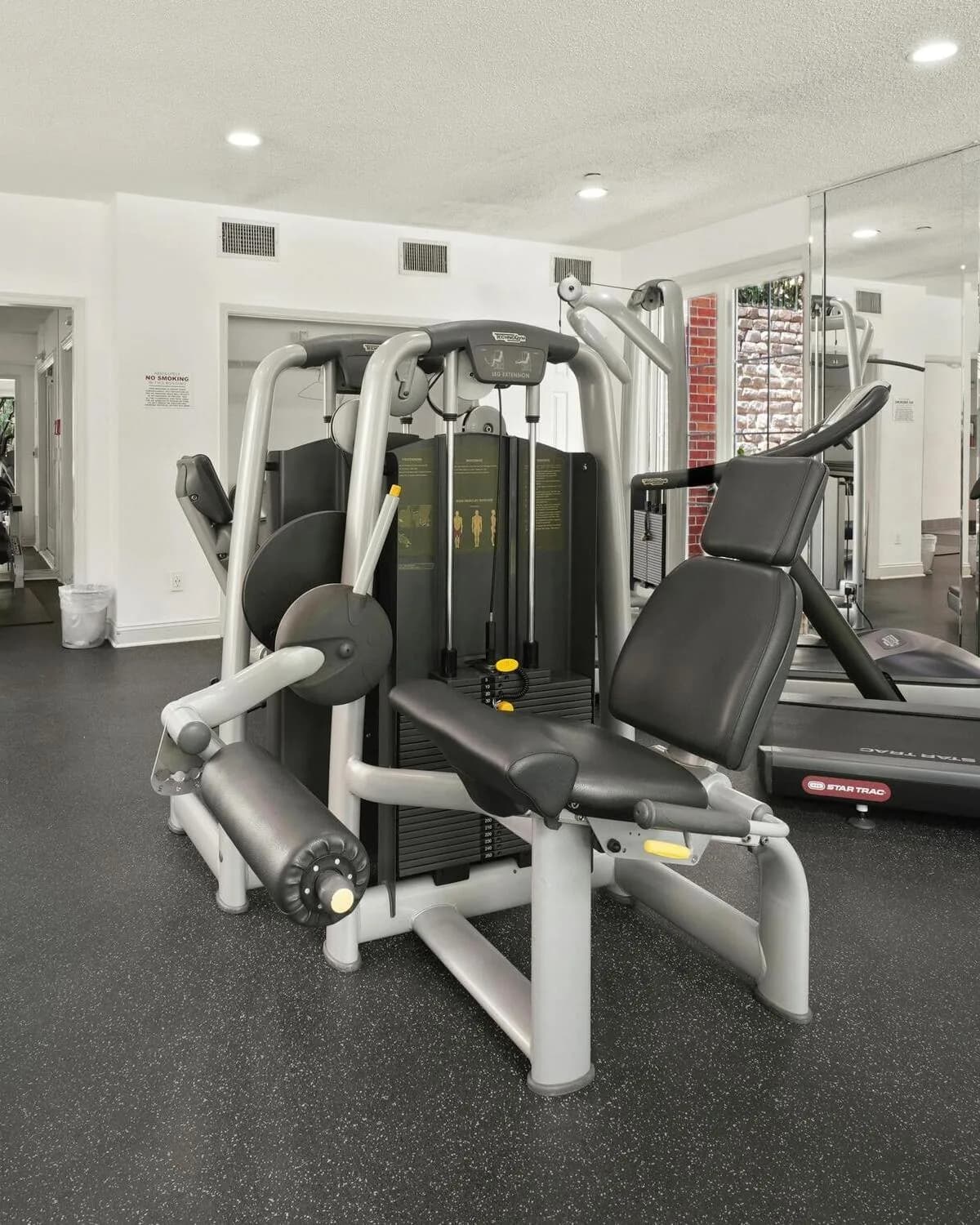 A fitness facility with a strength-training machine and a treadmill on rubber gym flooring