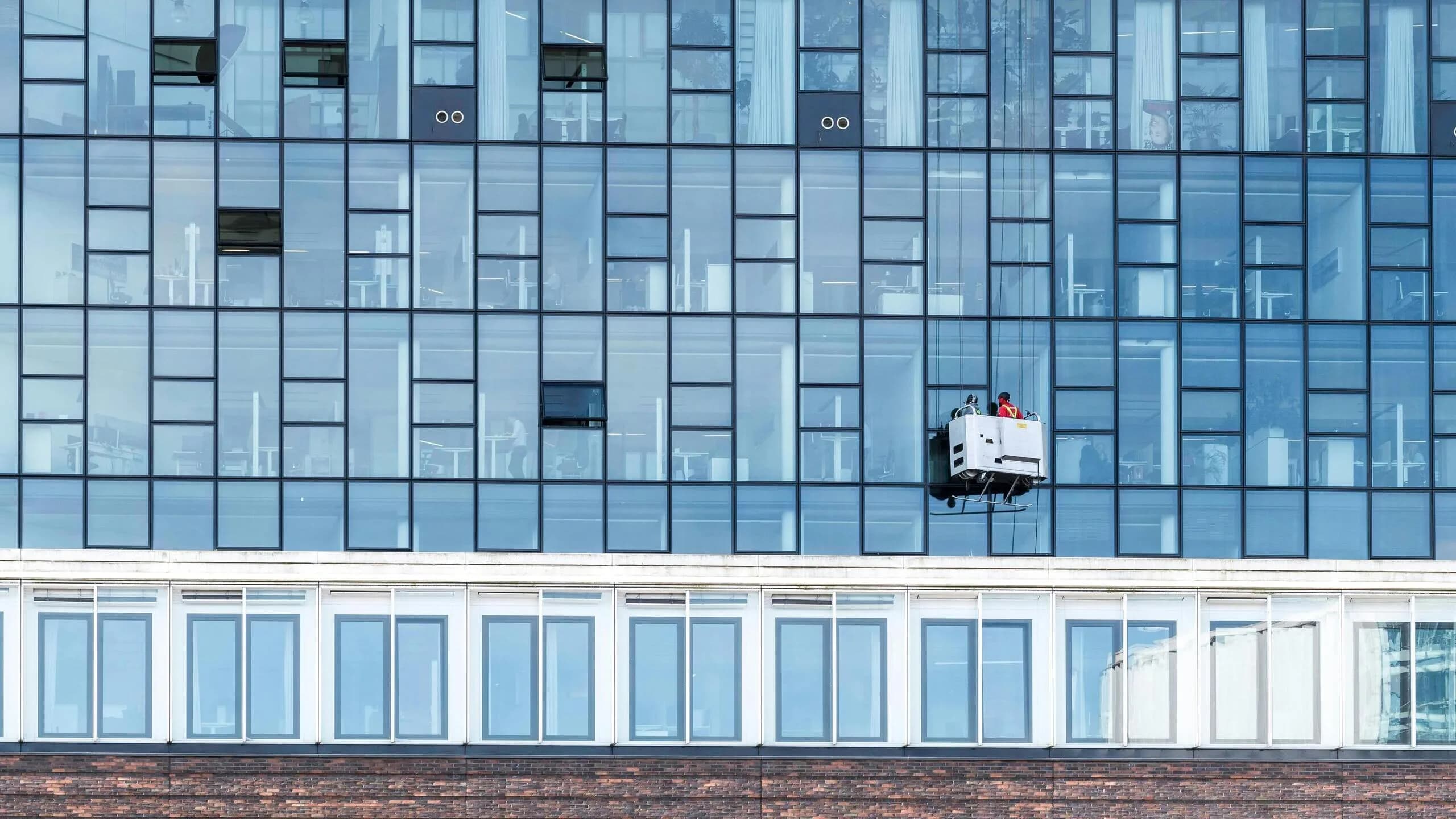 A window-cleaning gondola suspended against the glass curtain wall of a commercial high-rise