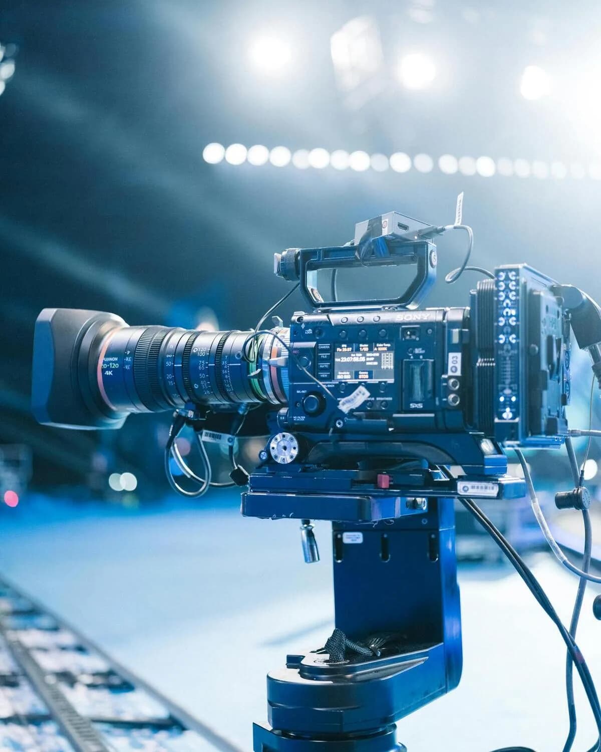 A professional cinema camera mounted on a pedestal on a film set under stage lighting