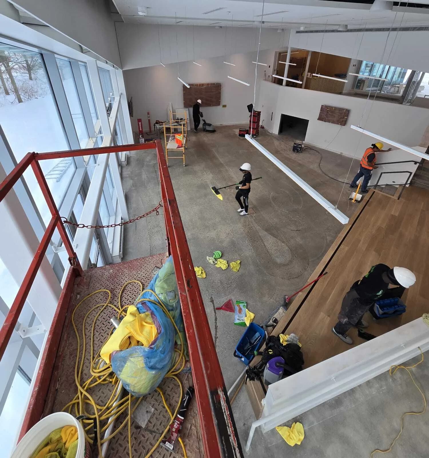 Overhead view of a cleaning crew in hard hats clearing and cleaning a large open commercial space during a post-construction job