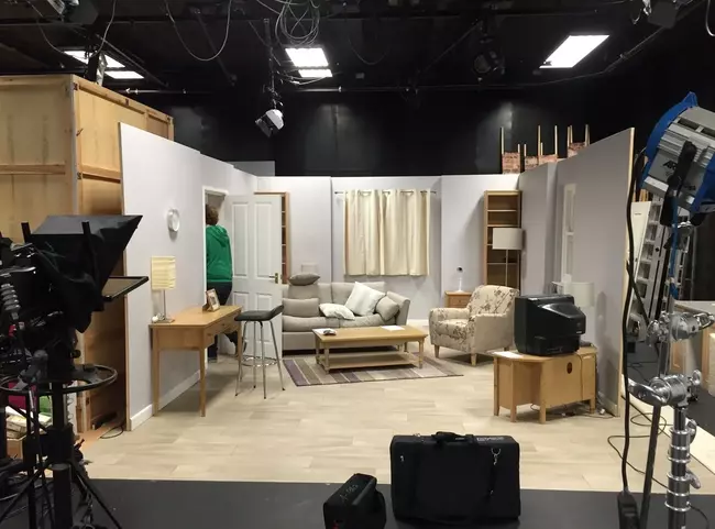 A dressed living-room film set with sofa, props and lighting rigs in a studio