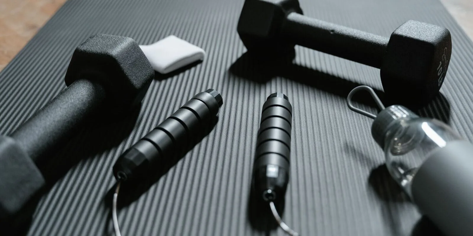 Dumbbells, jump ropes, a towel and a water bottle on a gym exercise mat